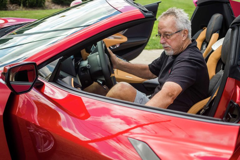 Old guy getting inside a red C8 Corvette convertible
